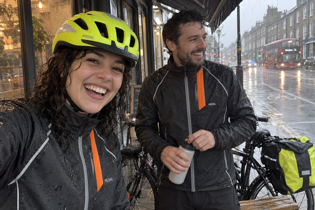 Two riders sheltering under a shop awning in heavy rain with their bikes, jackets beaded with water, waiting it out and laughing about it.